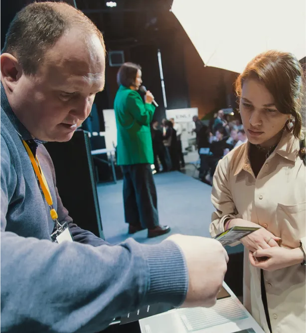 Специалист Gintereo показывает брошюру с межкомнатными перегородками из стекла и алюминия клиентке на выставке в Москве, СПБ